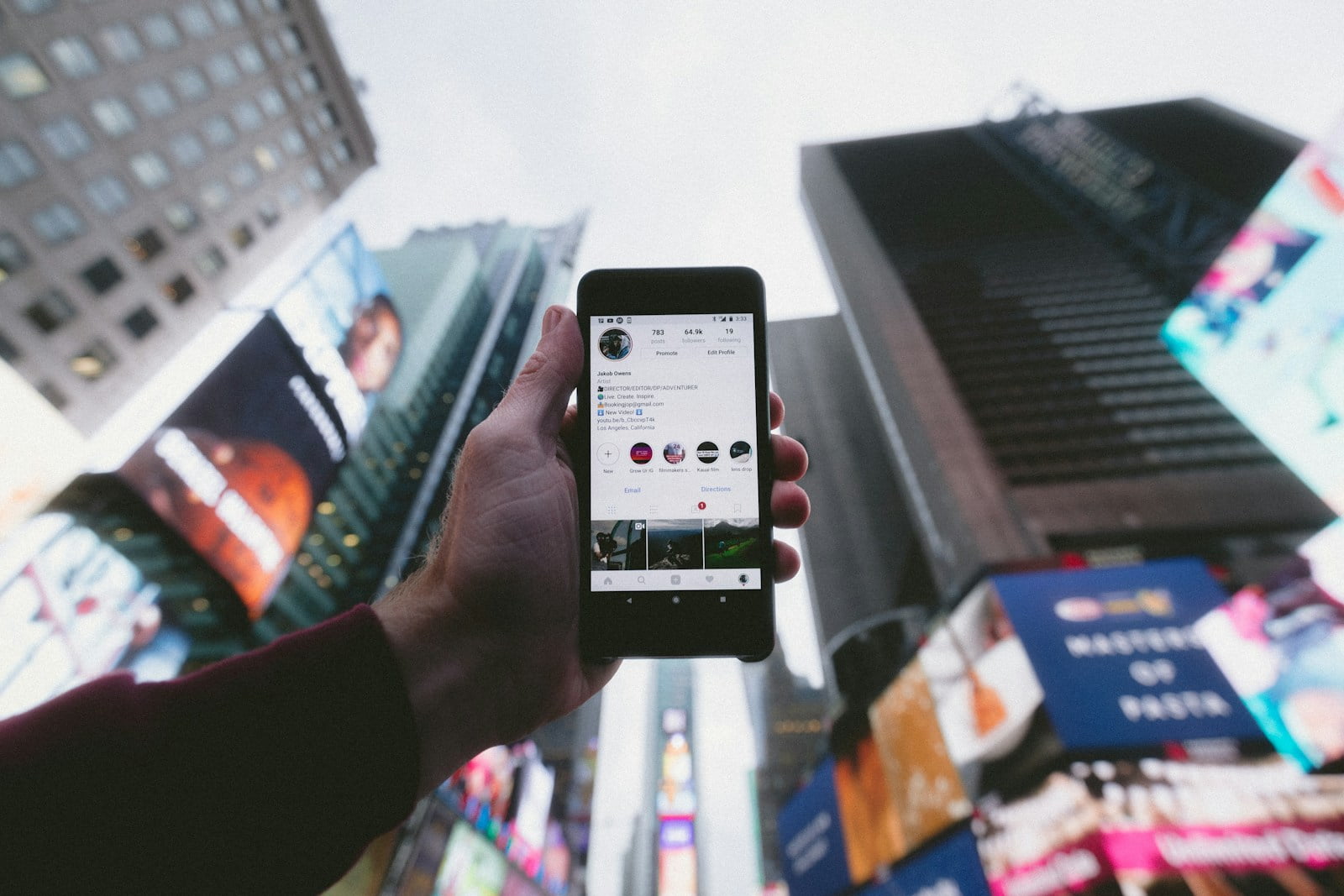 high angle photo of person holding turned on smartphone with tall buildings background representing pop culture and buzz words